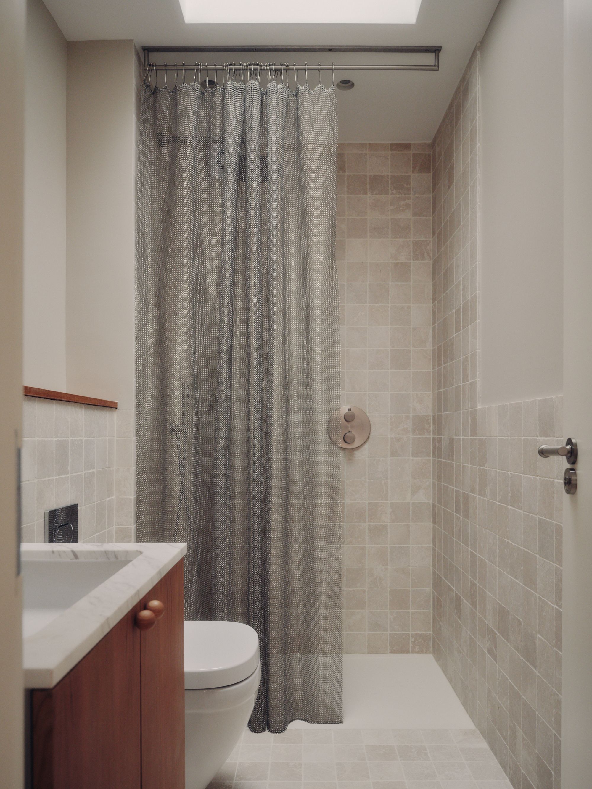 chainmail shower curtain in beige tiled bathroom with tiled floor, timber floating vanity, marble countertop and timber dado trim, and skylight
