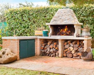 A brick outdoor barbecue in exterior space with logs for fuel