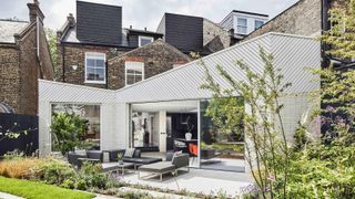 white clad single storey extension set at angle to house, with pitched sloping roofs coming downwards to central point, large sliding doors leading to patio and garden, brick semi detached property with loft conversions