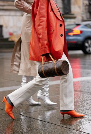 a close street-style photo of a woman carrying a vintage Louis Vuitton bag styled with an orange blazer, white jeans, and orange shoes