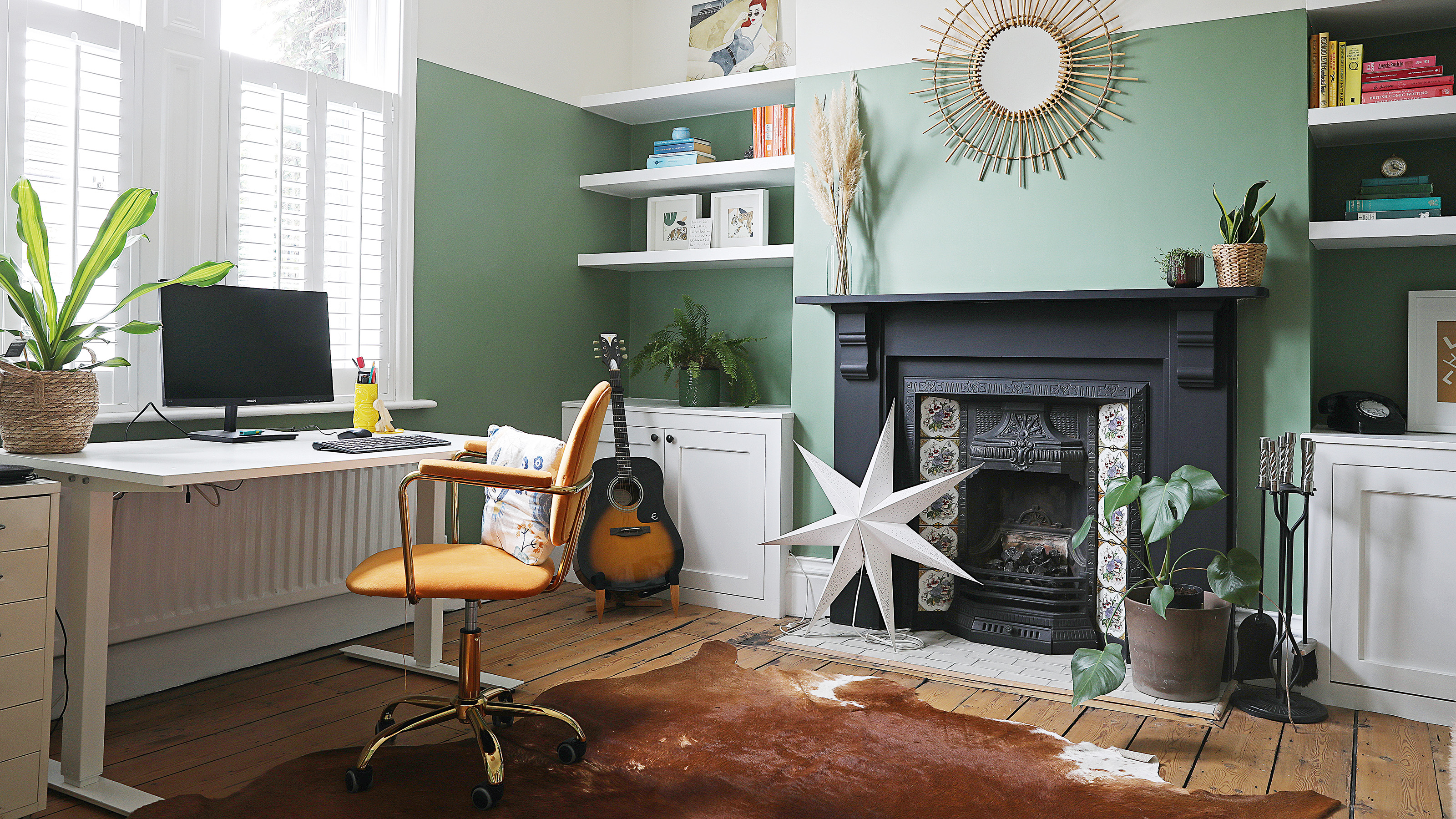 home office with desk positioned by the window with green walls, brown desk chair and victorian-style fireplace with alcove storage either side