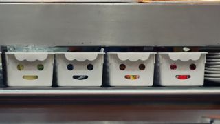 Plastic storage baskets on a shelf with what appears to be smiling faces formed by holes in one of their sides
