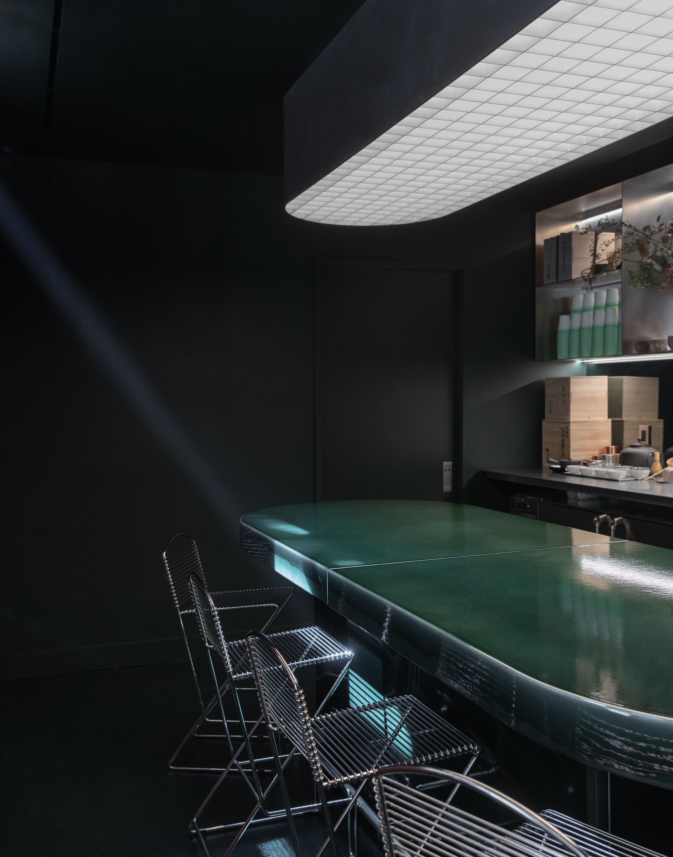 A futuristic matcha cafe features Japandi interiors punctuated by wood, chrome, or emerald green tones, and a sci-fi-esque bar setup with dripping water bottles and lights.