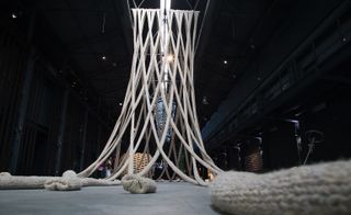 A giant web of knitted wool yarn cascades from the ceiling