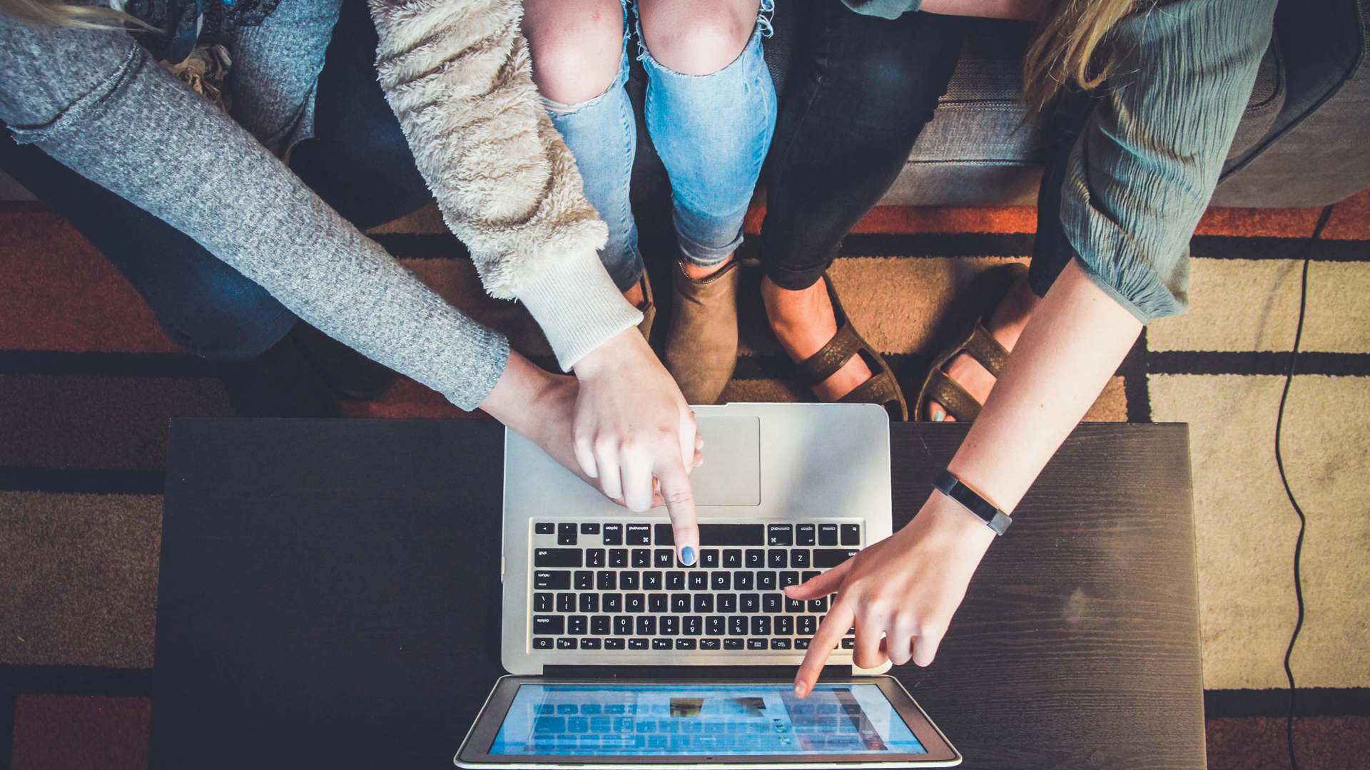 three people sat working on the same laptop