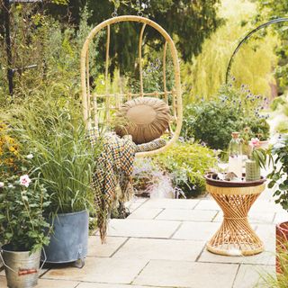 Bohemian patio garden with hanging rattan egg chair, rattan side table, and lots of potted plants