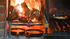 side shot of a roaring fire with grills and cast-iron skillets filled with preparations