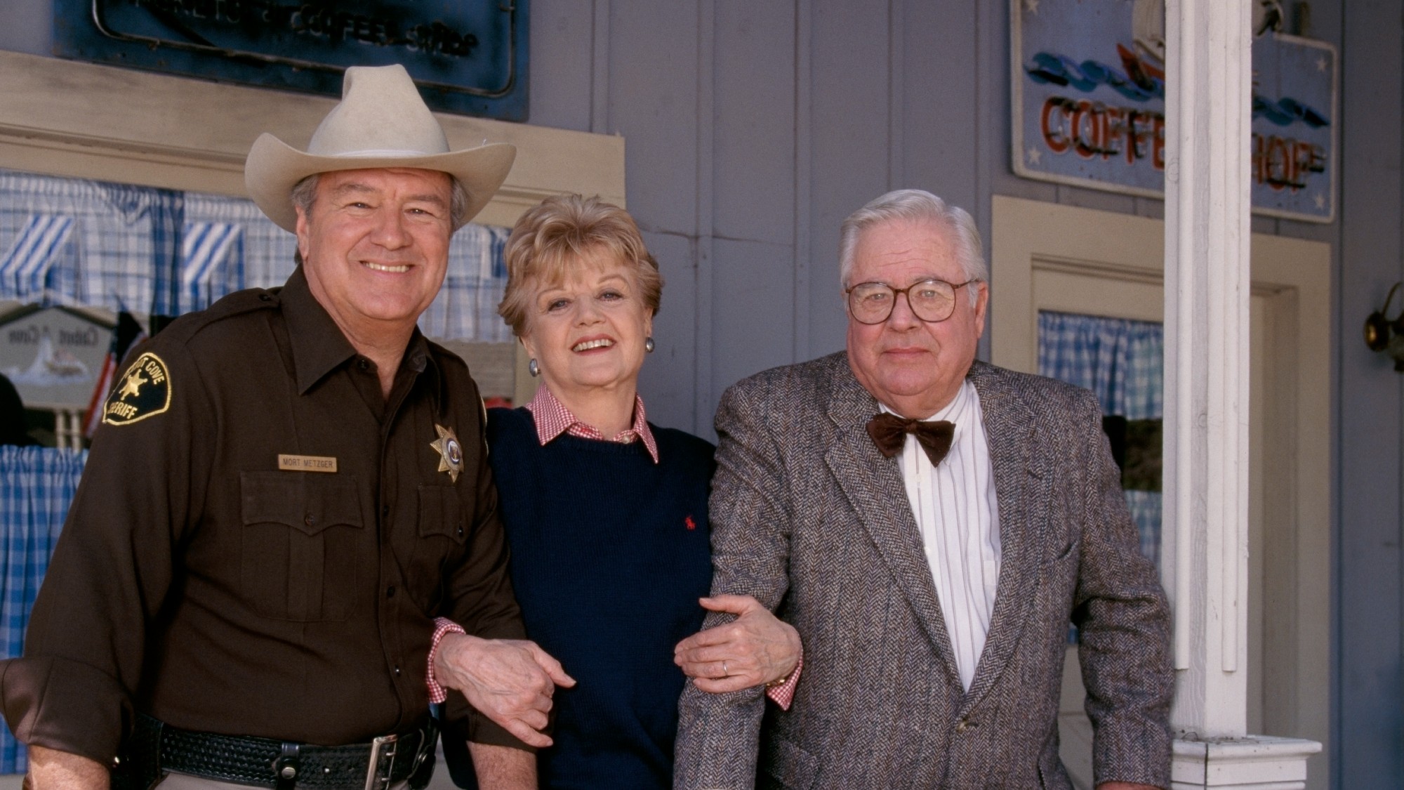 Angela Lansbury, smiling on a porch and arm-in-arm with two of her costars on the show 'Murder, She Wrote'