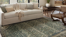 a living room with a cream couch, several pillows, a wooden accent chair, and a green, vintage-inspired rug