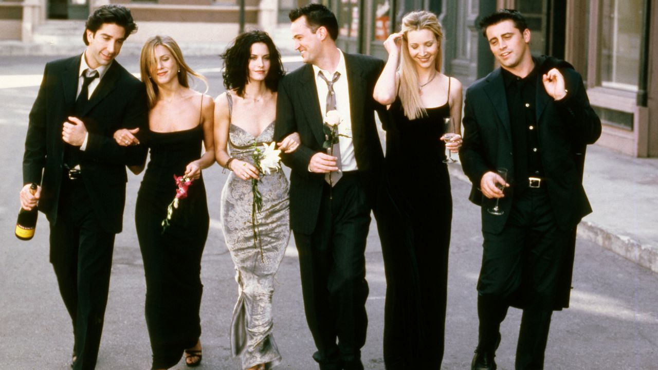 The cast of Friends walking down a NYC street in black dresses and suits