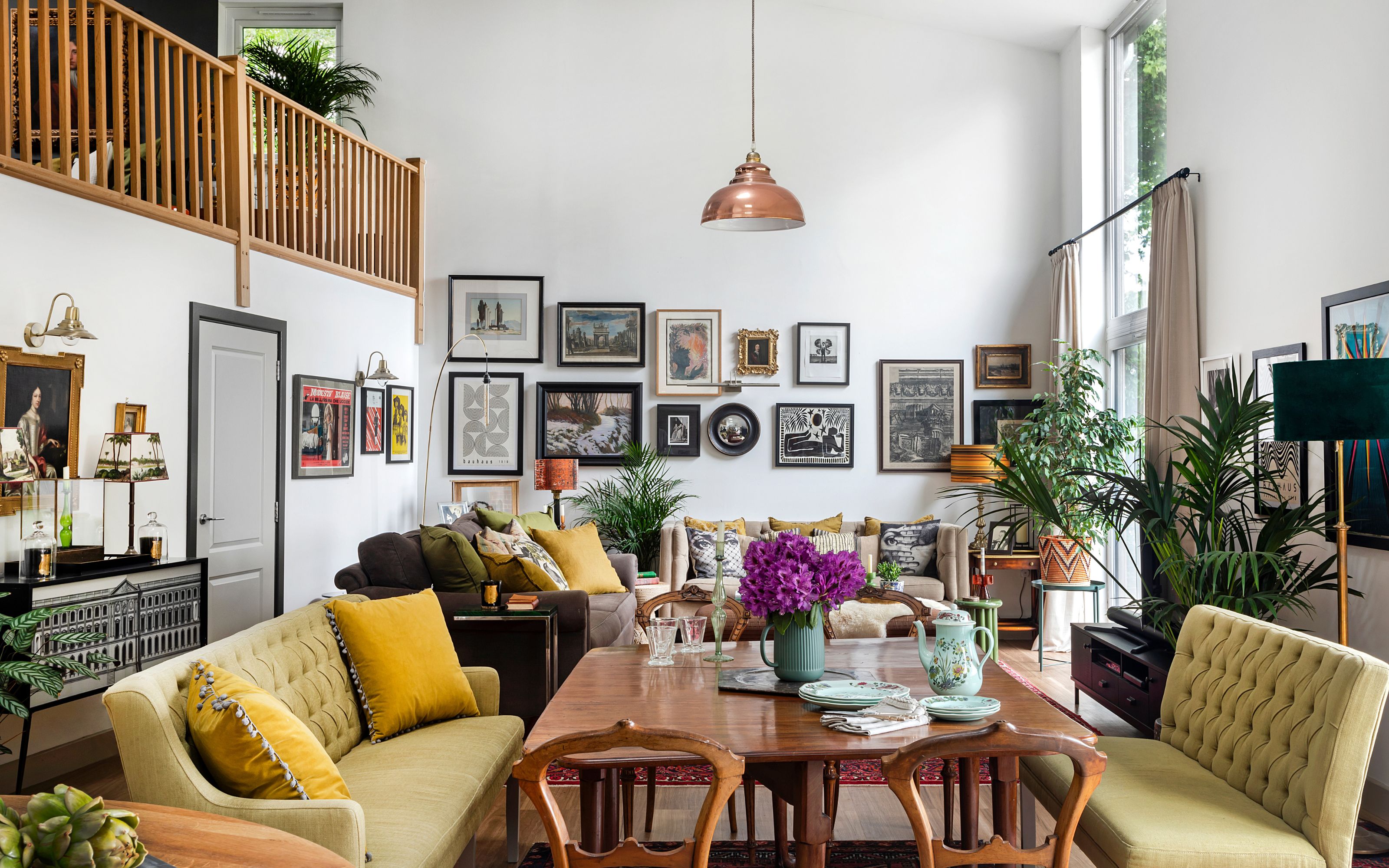 Dining room with open plan layout and mezzanine floor, gallery wall and wooden table and chairs with green sofa benches