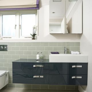 bathroom with grey wall tiles and wash basin with mirror and drawers
