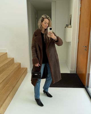 Anouk is wearing a brown coat, blue jeans, black ysl bag, and black kitten heel boots.