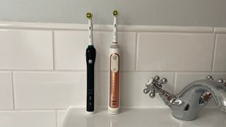 Two Oral B toothbrushes side by side on a bathroom sink.