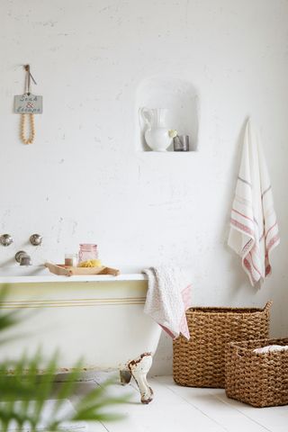 All white bathroom with a freetstanding bath and wicker baskets used as bathroom storage