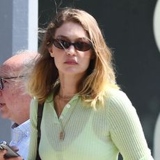 Gigi Hadid wearing brown loafers, white linen pants, and a sheer green top