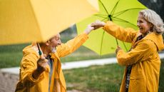 An older couple dance in the rain with umbrellas.