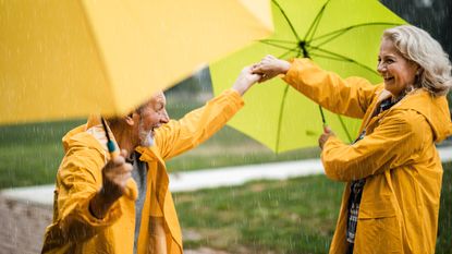 An older couple dance in the rain with umbrellas.
