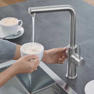Silver boiling water tap being used to add water to a cup of coffee