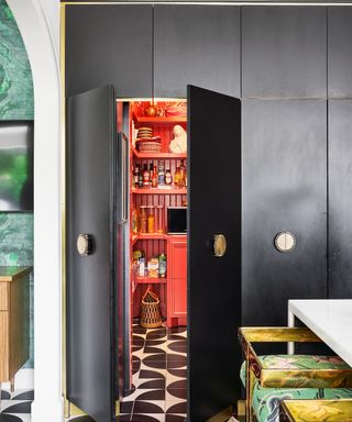 Brightly painted coral walk-in pantry, cleverly concealed and within bespoke black floor to ceiling kitchen cabinetry