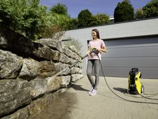 Woman using Kärcher K7 Premium smart control pressure washer to clean a stone wall