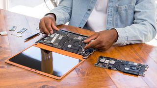 A man at a wooden table replacing the mainboard in his Framework Laptop.