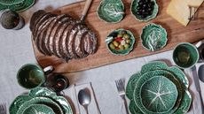 spring table laid with cabbageware plates bowls and charger plates with a large wooden serving board laden with bread and small bowls of olives