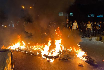 Protesters gather near a burning motorcycle as they take to the streets in anger over the death of Amini