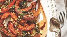 Plate of roasted squash with a green dressing next to a fork and spoon