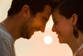 couple facing each other and smiling outdoors at sunset 