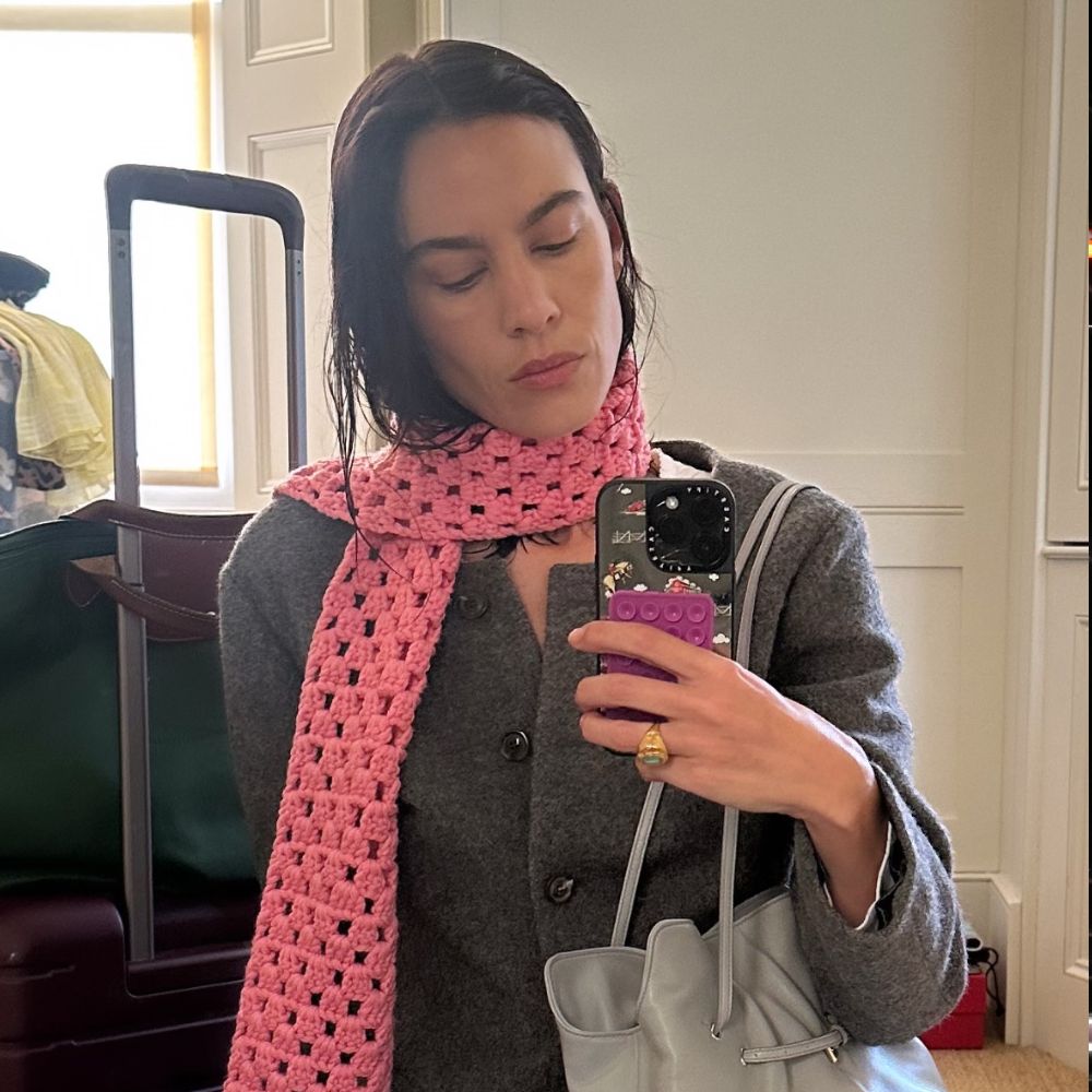 Alexa Chung takes a mirror selfie wearing the Prada Dada bag in grey with a grey blazer and white jeans.
