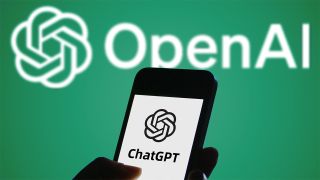 Smartphone displaying ChatGPT logo held in front of white OpenAI logo on green background
