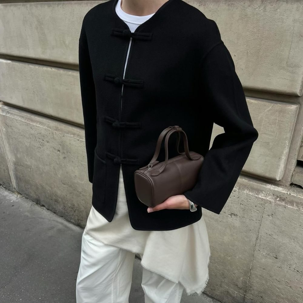 Woman wears black jacket, cream top, white trousers and brown bag 