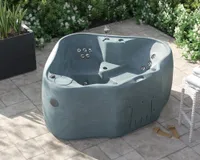 A small two-person grey hard-shell hot tub on a paved patio