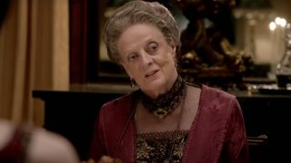 Dame Maggie Smith cocks her head as she speaks at the dinner table in Downton Abbey.