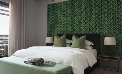 Hallmark House bedroom with white linen and green headboard. There is a green ottoman with two books on it.