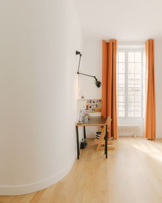 Study with desk, a lamp mounted to the wall and orange curtains in the Le Marais apartment