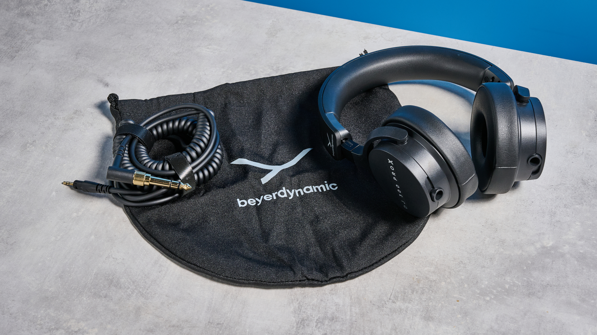 the beyerdynamic DJ 300 Pro X headphones in black showing their ear cups, carry bag, and connectivity options photographed against the blue tom's guide background