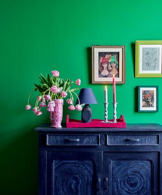 Bright entryway with green painted wall, black cabinet with pink decorative tray, styled with flowers, candles and ornaments