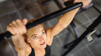 Woman looks up at a pull-up bar she is holding on to