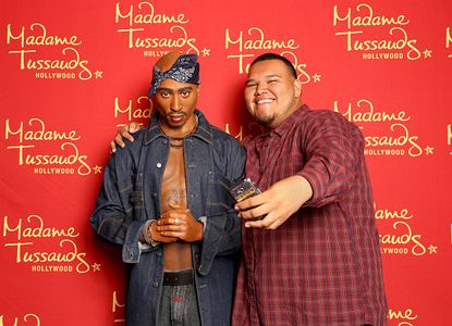 A man poses with a wax figure of Tupac Shakur.