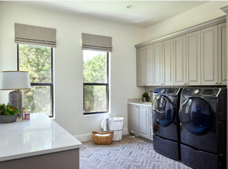 Laundry room with quartz countertops and tiled flooring. There are two washing machines in the space with overhead cabinets.