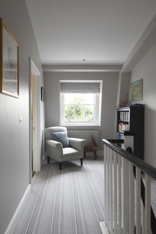 Landing with striped carpet and neutral walls with armchair and bookcase by window