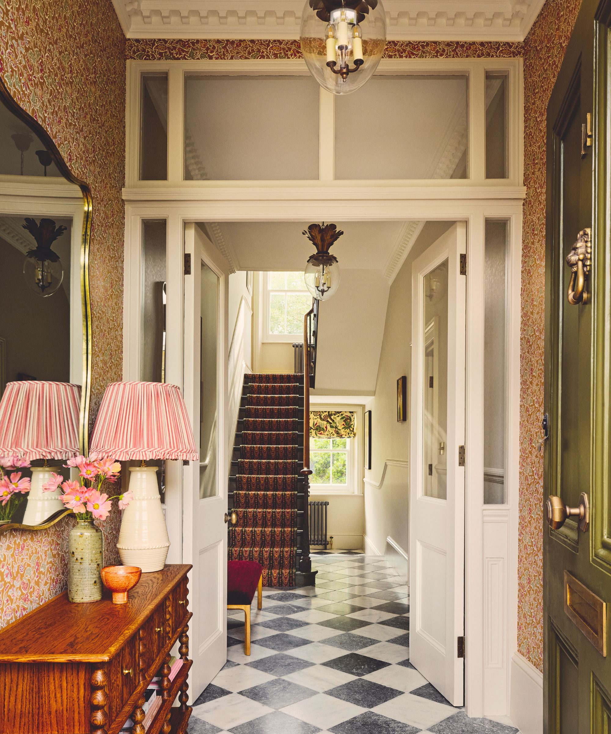 small floral patterned orange toned wallpapered entryway with a black and white checkerboard floor and green front door