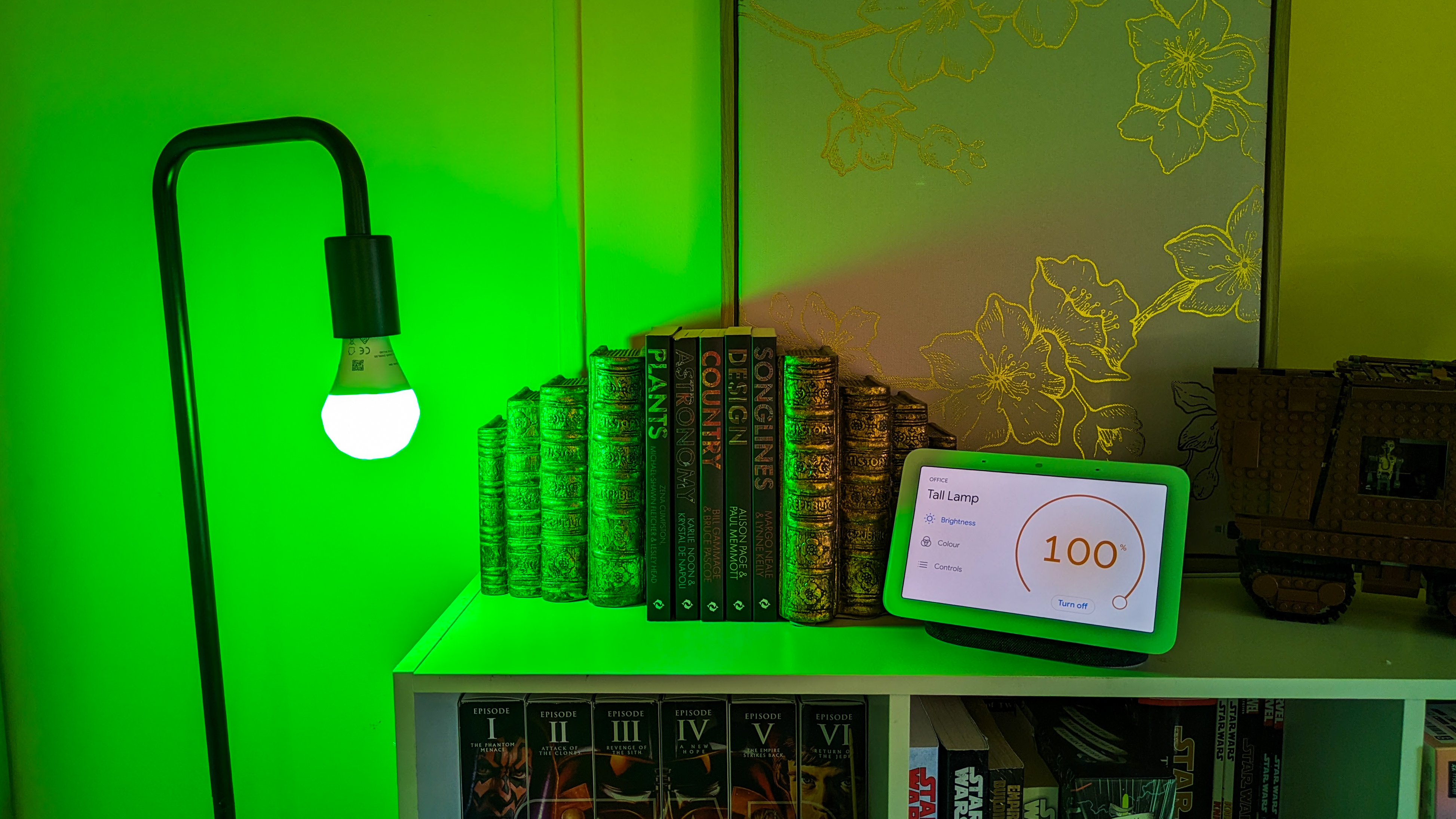 Nanoleaf Essentials smart bulb with green light next to Google Next Hub 2 showing it's at maximum brightness