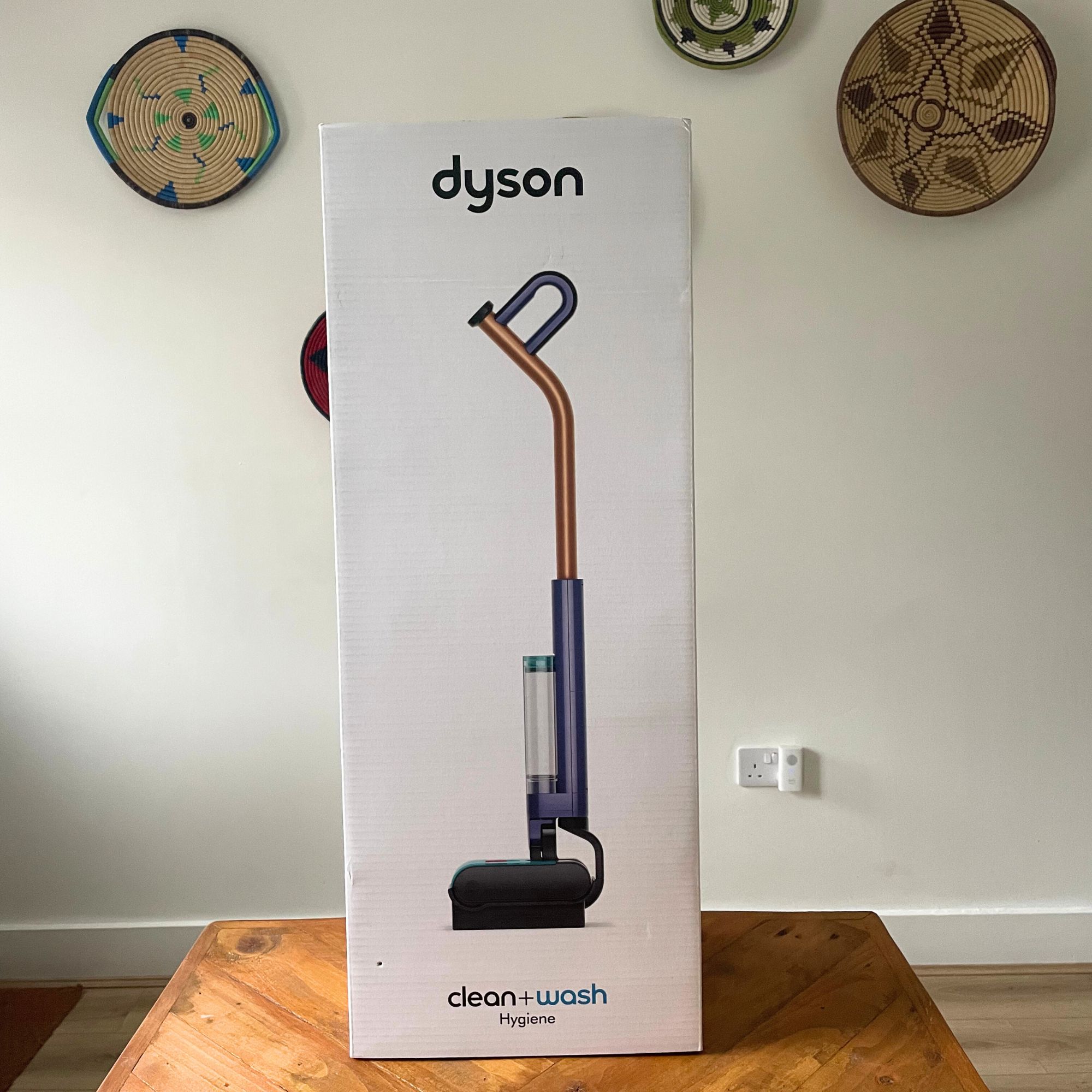 Dyson Clean+Wash Hygiene sitting on a wooden table in front of a white wall
