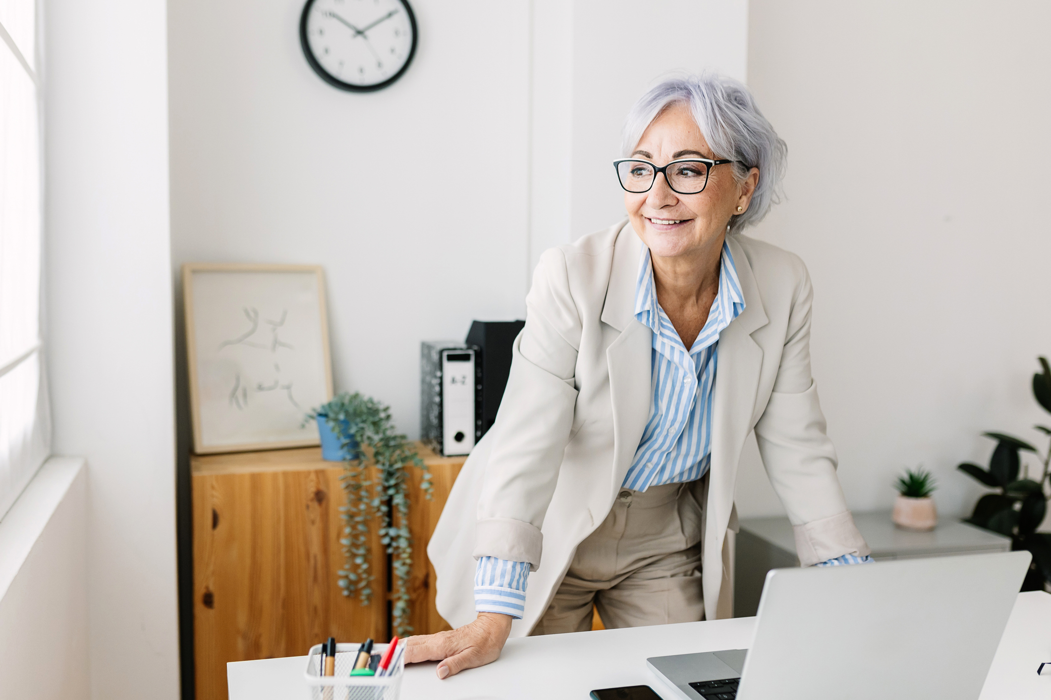Happy mature middle aged businesswoman working on laptop computer at modern office workplace.