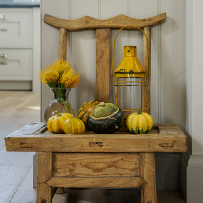 Small ethnic wooden chair with a display of pumpkins and a vase of yellow flowers. An oak framed new build, a cottage style bungalow home of retired couple Sheila and Geoffrey McGaughey in Surrey