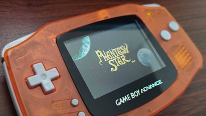 Close up of transparent orange Game Boy Advance with backlit screen and Phantasy Star start screen displayed.