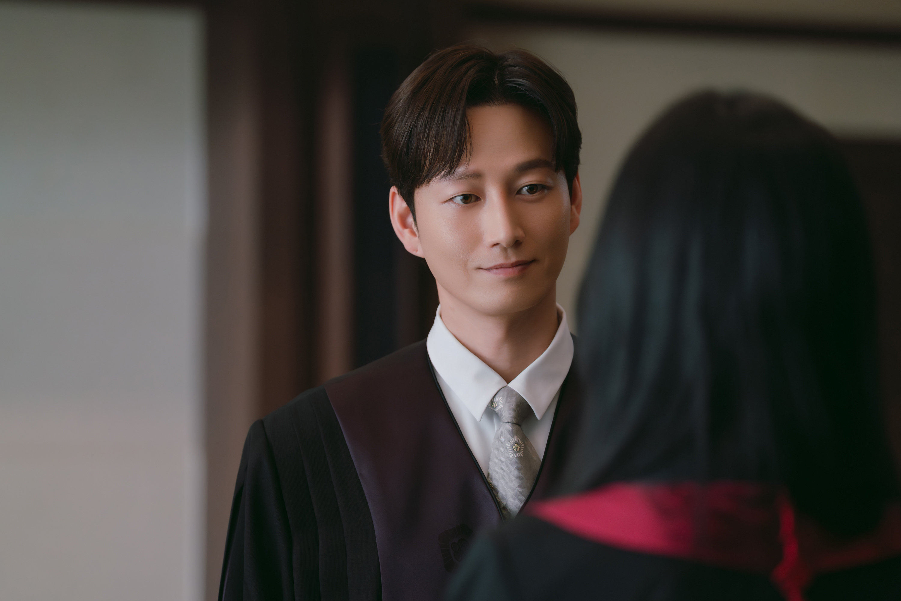 A man in a Korean judge's robe (Kim Hyun-wook as the Judge Boyfriend) stands in front of a female attorney, in the Netflix K-drama 'Boyfriend on Demand.'